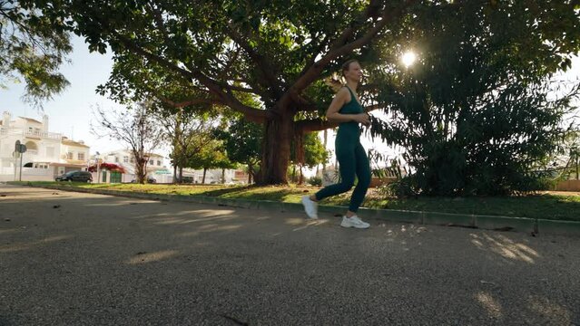 girl  jogs through a park early in morning, running in shade of trees.The sun filters through tree canopy, casting dappled light. camera captures scene from a low, wide-angle perspective