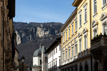 Obraz premium View of buildings and the Cathedral Tower in a sunny day in Trento city centre. Dolomites in background; Trentino-Alto Adige, Italy