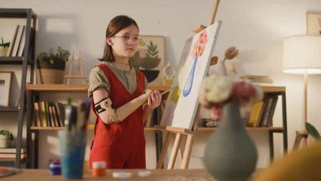 Selective focus footage of Caucasian little girl in glasses painting still life using right hand with prosthesis at cozy home