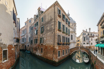 Typical narrow canal surrounded by buildings with boats and a footpath bridge in Venice, Veneto,...
