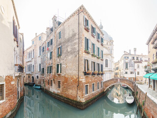 Typical narrow canal surrounded by buildings with boats and a footpath bridge in Venice, Veneto,...