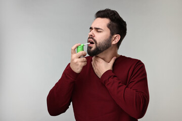 Young man using throat spray on grey background