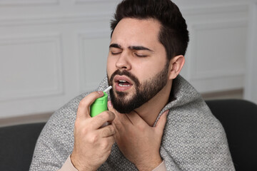 Young man using throat spray at home