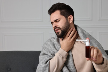 Young man holding throat spray indoors. Space for text