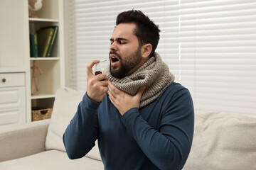 Young man with scarf using throat spray indoors