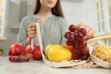 Woman taking grapes out from string bag at light marble table, closeup