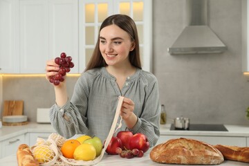 Woman taking grapes out from string bag at light marble table