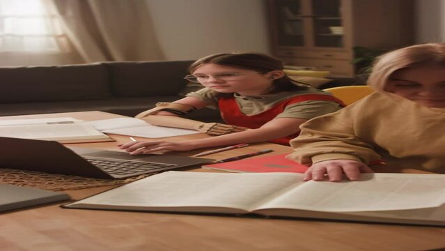 Vertical side footage of Caucasian schoolgirl with artificial arm doing homework together with mom using laptop