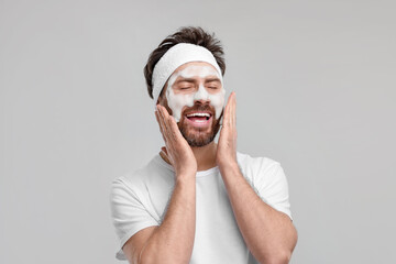 Man with headband washing his face on light grey background