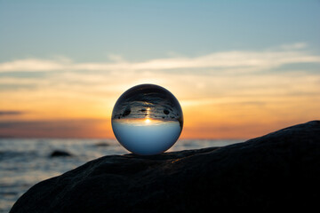 Ball made of glass lies on a stone in which the beach and the sea are reflected