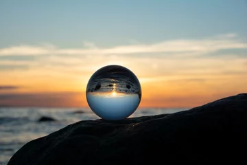 Foto op Plexiglas Ball made of glass lies on a stone in which the beach and the sea are reflected © Claudia Evans 