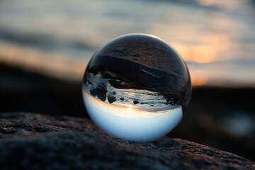 Glass  ball lies on a stone in which the beach and the sea are reflected