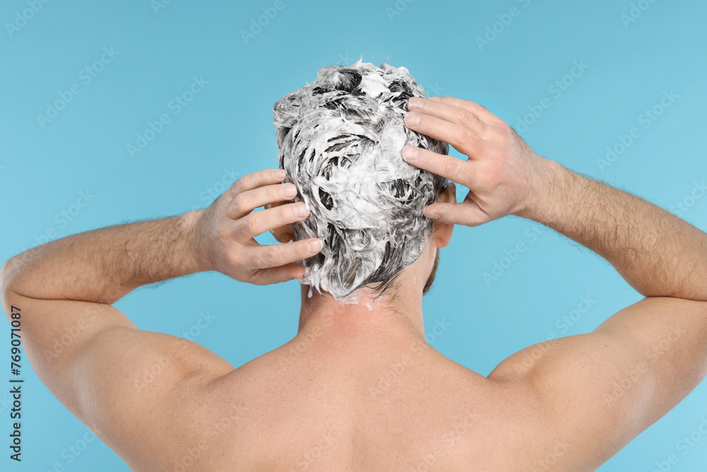 Sticker man washing his hair with shampoo on light blue background, back view