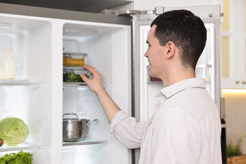 Happy man taking containers with vegetables out of refrigerator in kitchen