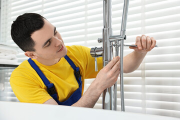 Young plumber repairing faucet with spanner in bathroom
