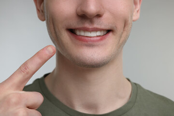 Young man showing his teeth with whitening strip on light grey background, closeup