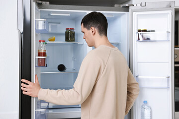 Man near empty refrigerator in kitchen at home
