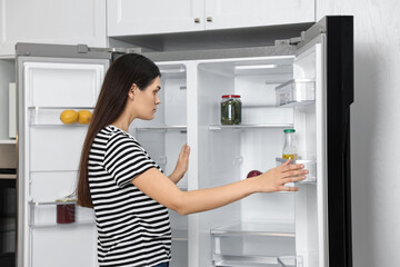Fototapeta na wymiar Upset woman near empty refrigerator in kitchen