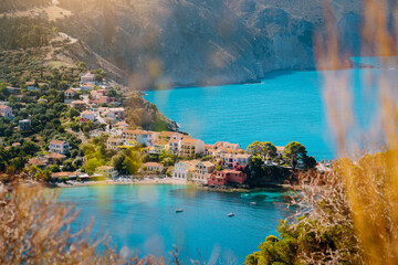 Framed by summer nature plants view to Assos village Kefalonia. Beautiful blue colored bay lagoon water surrounded by cliff, rocks, pine and cypress trees. Greece