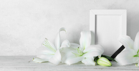 Blank funeral frame and beautiful lily flowers on table