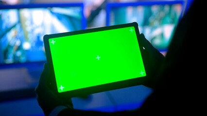 Man security guard officer in monitoring center holding tablet with chroma key green screen....