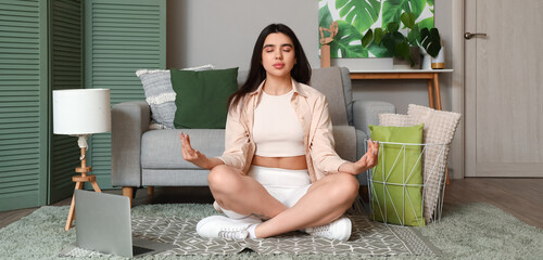 Young woman meditating with laptop at home