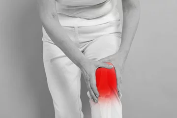 Deurstickers Arthritis symptoms. Woman suffering from pain in her knee on background, closeup. Black and white effect with red accent in painful area © New Africa
