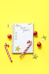Notebook with empty to do list, candy canes and Christmas balls on yellow background. New year goals