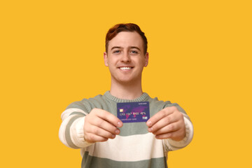 Young man with credit card on yellow background