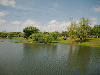 Obraz premium Wide horizontal view over urban lake at Booker Creek Park in St. Petersburg, FL On a sunny day. Sunshine and shade. Green grass and trees with blue sky and reflections Room for copy no people. 
