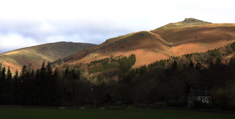 Butter Crag near Grasmere. A drab day in Winter is brightened by sunlight on the upper fells.