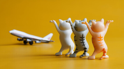 Three toy kittens with raised paws and passenger airplane on yellow background. Concept of seeing...