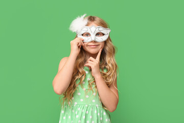 Thoughtful little girl wearing carnival mask on green background