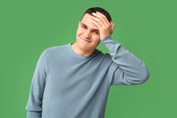 Handsome ashamed young man covering face with hand on green background