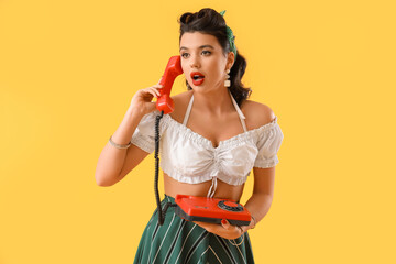 Attractive pin-up woman talking by telephone on yellow background