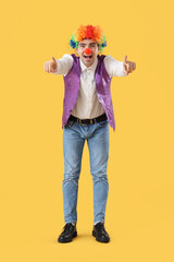 Happy young man in clown costume pointing at viewer on yellow background