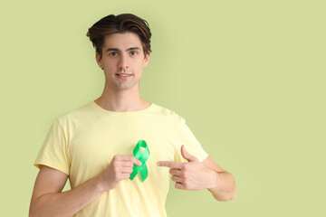 Young man pointing at green ribbon on color background. Glaucoma awareness month