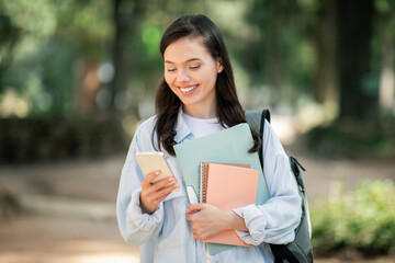 Fototapeta premium Engaged young female student with a cheerful expression, using a smartphone