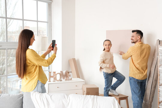 Happy family hanging painting in room on moving day