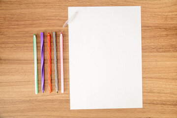Canetas coloridas e papel branco A4 para escrita, com tampa sob fundo de madeira