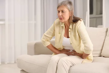 Schilderijen op glas Menopause. Woman suffering from abdominal pain on sofa at home, space for text © New Africa