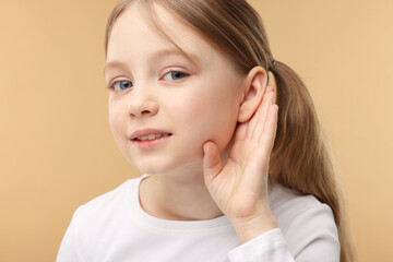 Little girl with hearing problem on pale brown background