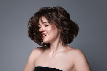 Obraz premium Portrait of beautiful young woman with wavy hairstyle on grey background