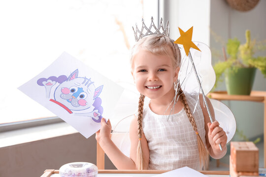Cute little girl dressed as fairy with drawing at home