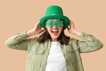 Happy young woman in leprechaun hat and stylish decorative glasses in shape of clover on brown...