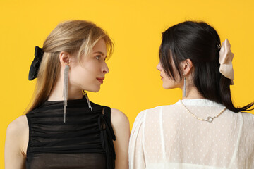 Fototapeta premium Beautiful young women with bows on their hair and different stylish jewelry on yellow background