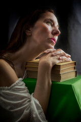 woman in a white blouse with a Carmen neckline with her hands resting on an old book in a romantic attitude V
