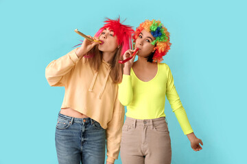 Beautiful young women in funny clown disguise with party whistles on blue background. April Fools...