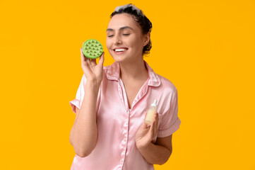 Beautiful young woman with hair scalp massager and bottle of cosmetic oil on yellow background