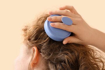 Young woman using hair scalp massager on beige background, closeup